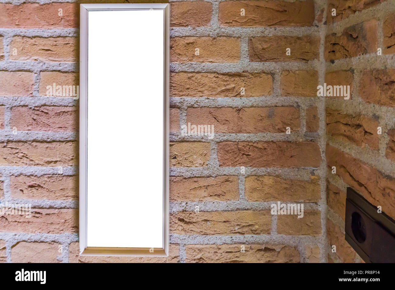 empty small long rectangular picture frame hanging on a brick wall close to a corner Stock Photo