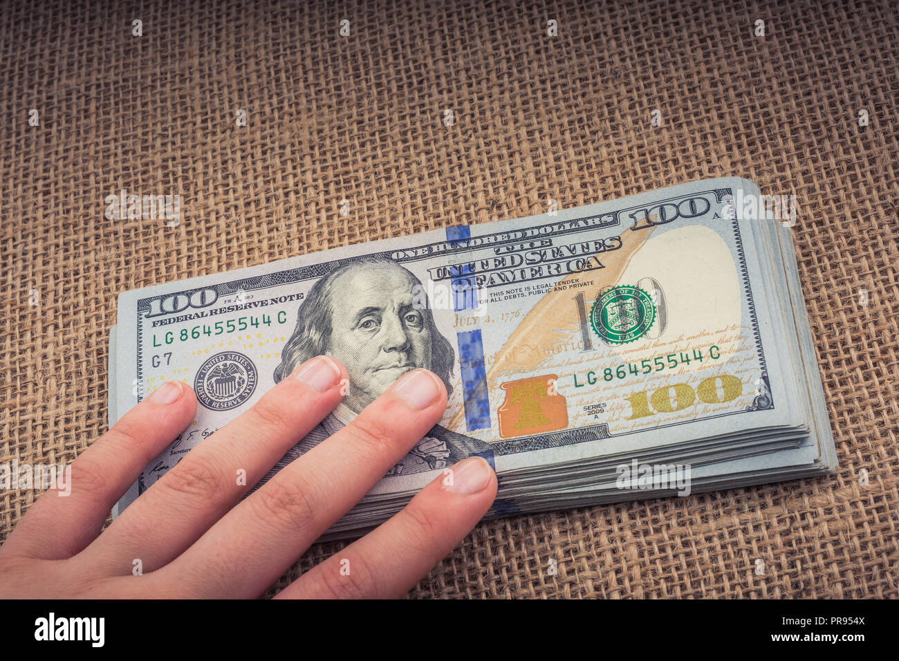 Hand holding banknote bundle of US dollar on a linen canvas background ...