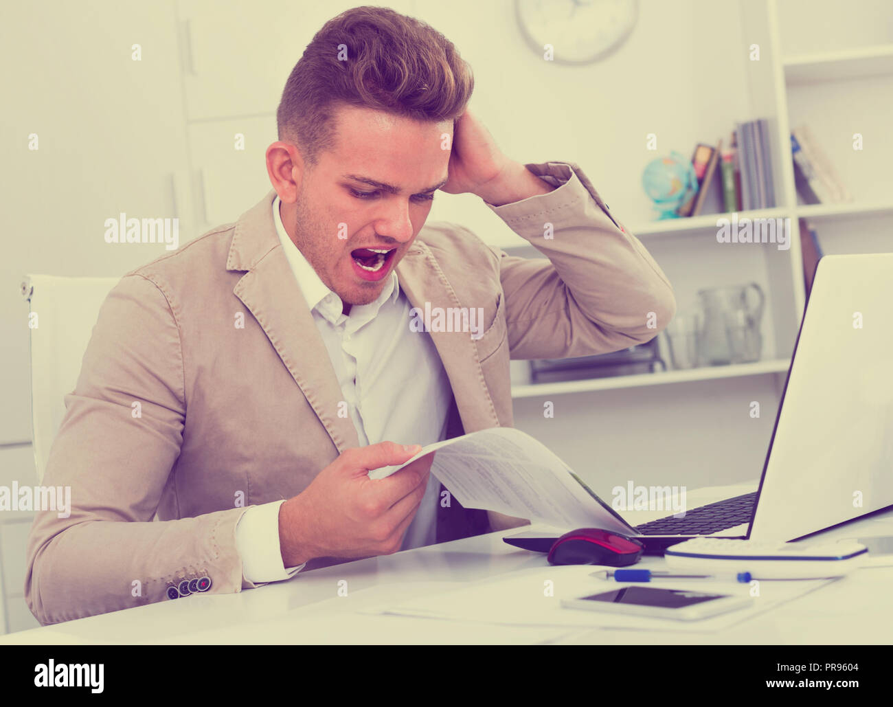 Upset young man having business problems with documents at workplace Stock Photo