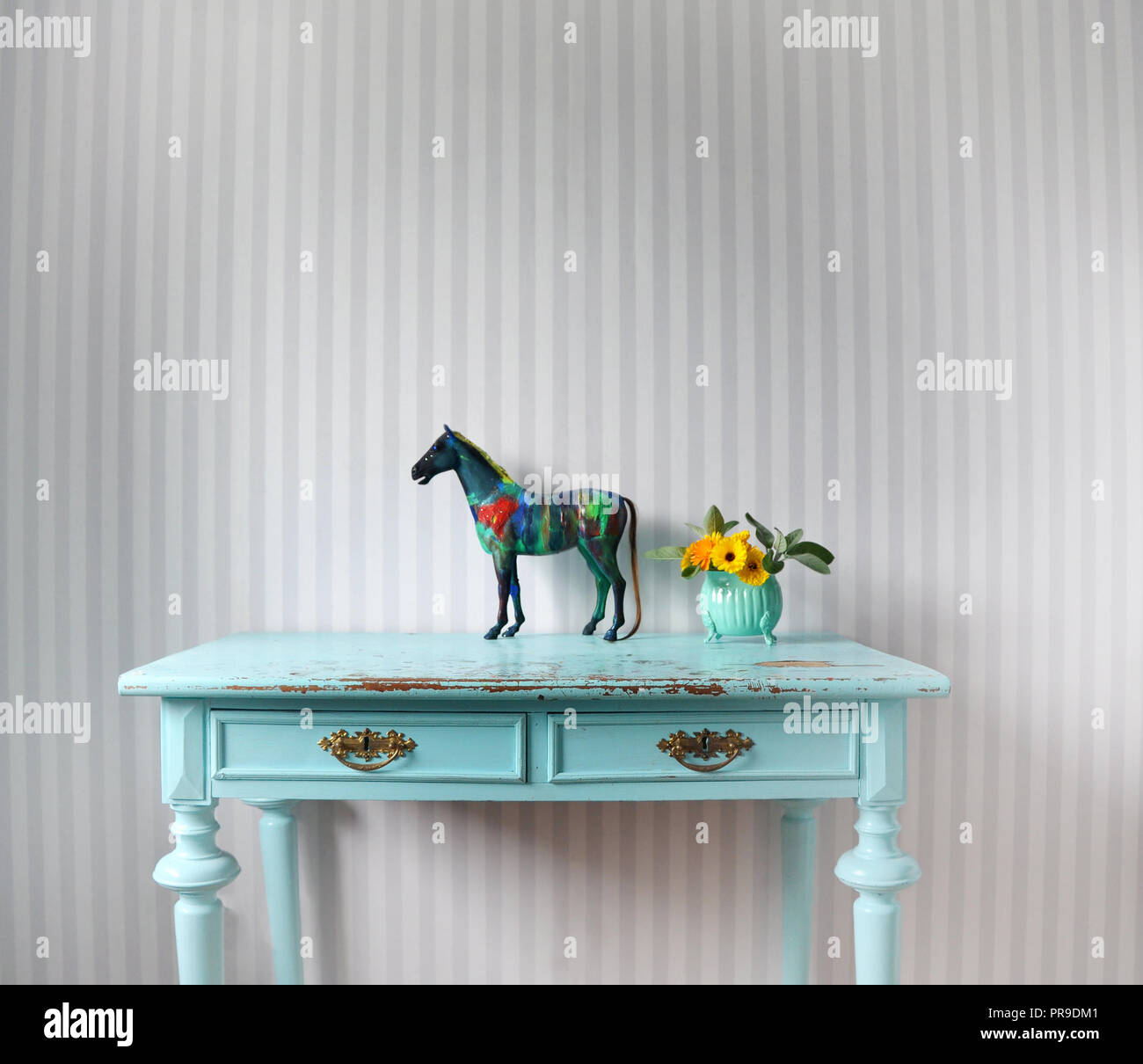 Vintage interior - Turquoise desk and grey striped wallpaper. Recycled plastic horse made new with acrylic colors. Marigolds in a vase. Stock Photo