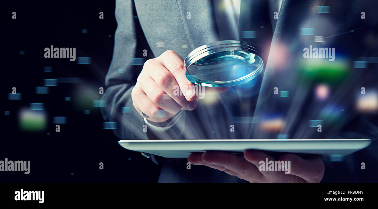 Businessman examines a tablet with a magnifying glass. Concept of internet security Stock Photo