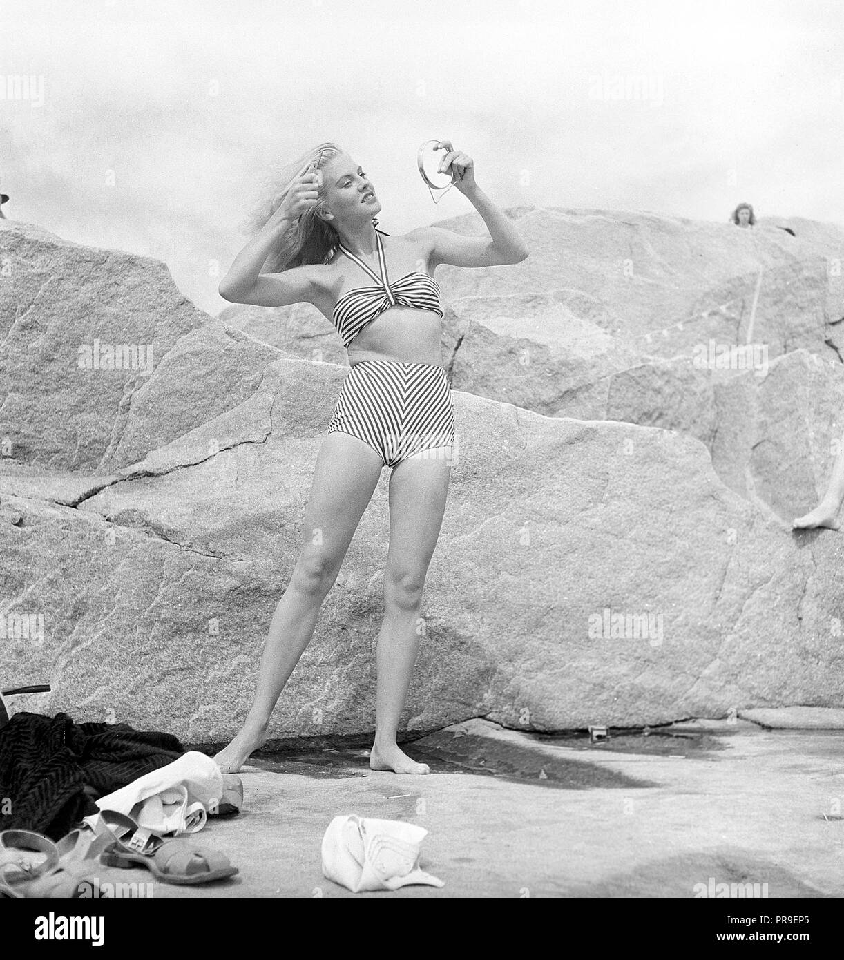 1940s bikini fashion. It's a sunny day and the blonde young woman is  wearing a typical 1940s two piece bathing suit or bikini. The pattern of  the fabric is an eyecatching design