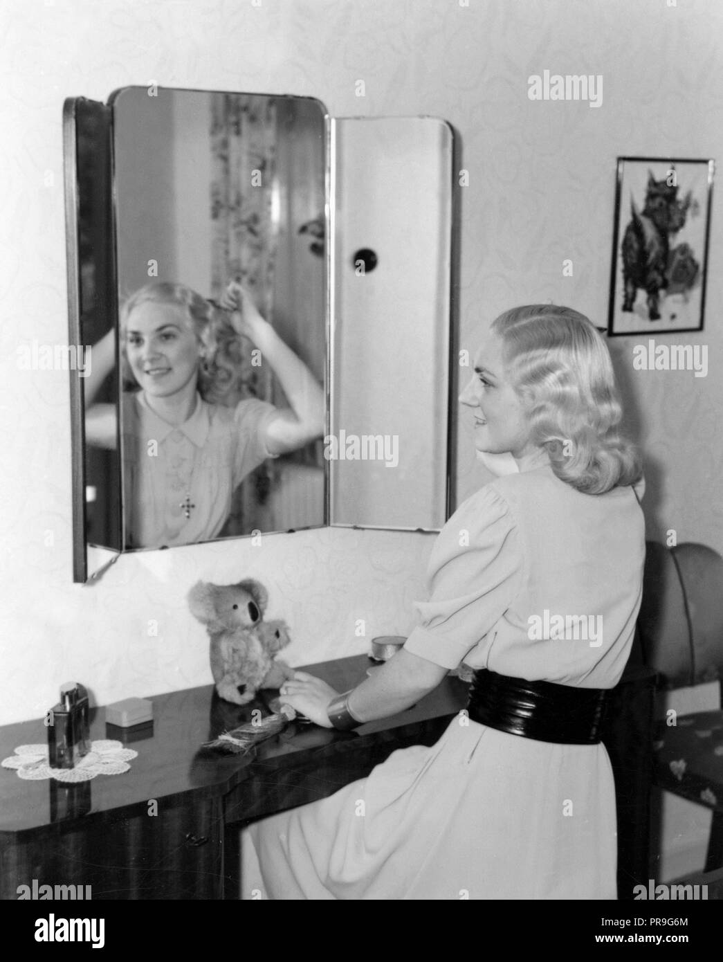 Cosmetics in the 1940s. Young opera singer Inge-Gerd Norlin at home in front of a mirror. The blonde young woman wears a light brightcolored dress with a wide black belt around the waist. She has a nice 1940s hairdo and combs her blonde hair in front of the mirror. Sweden 1940s Stock Photo