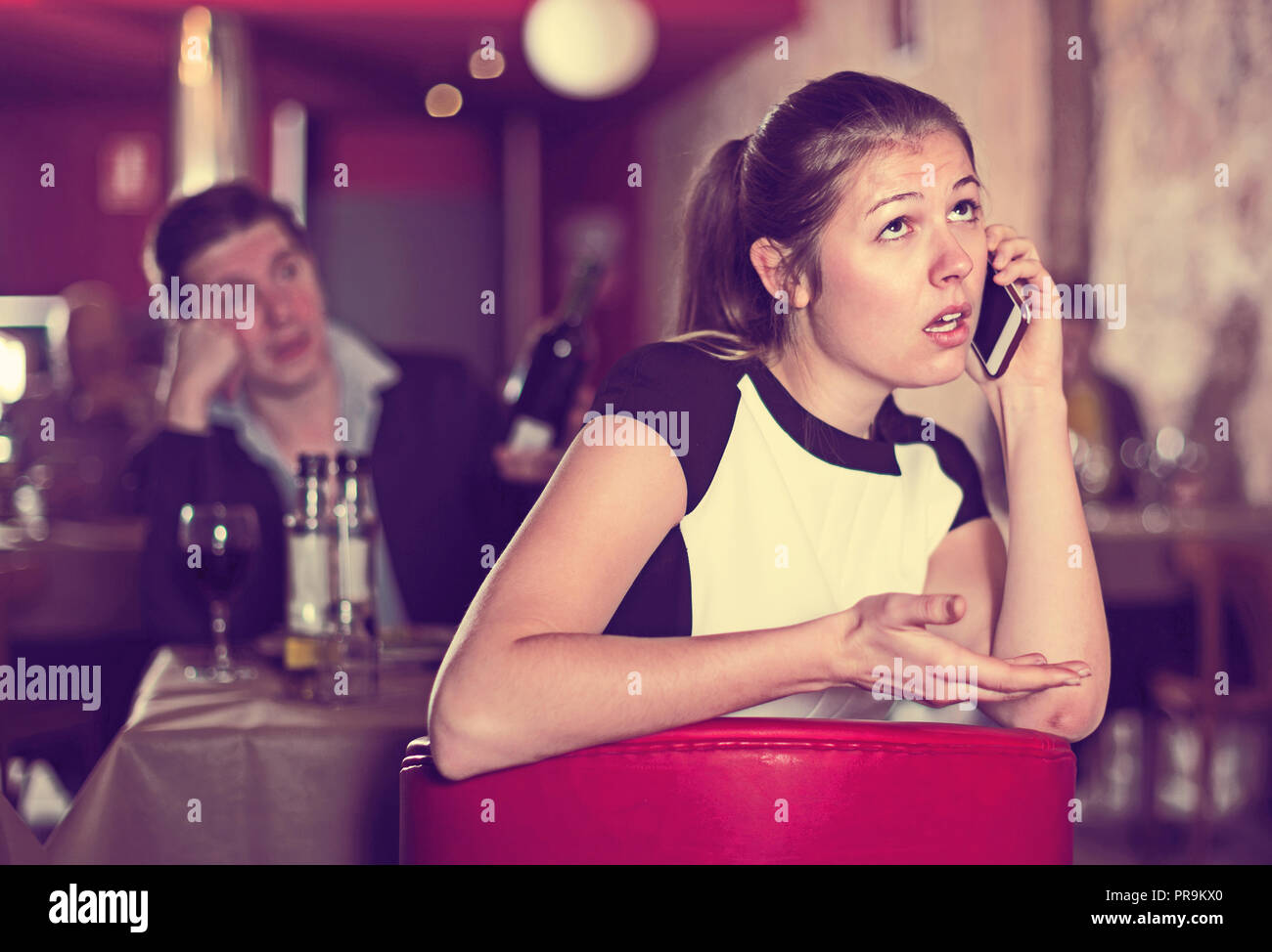 Unhappy young woman talking on mobile phone sitting apart in restaurant ...