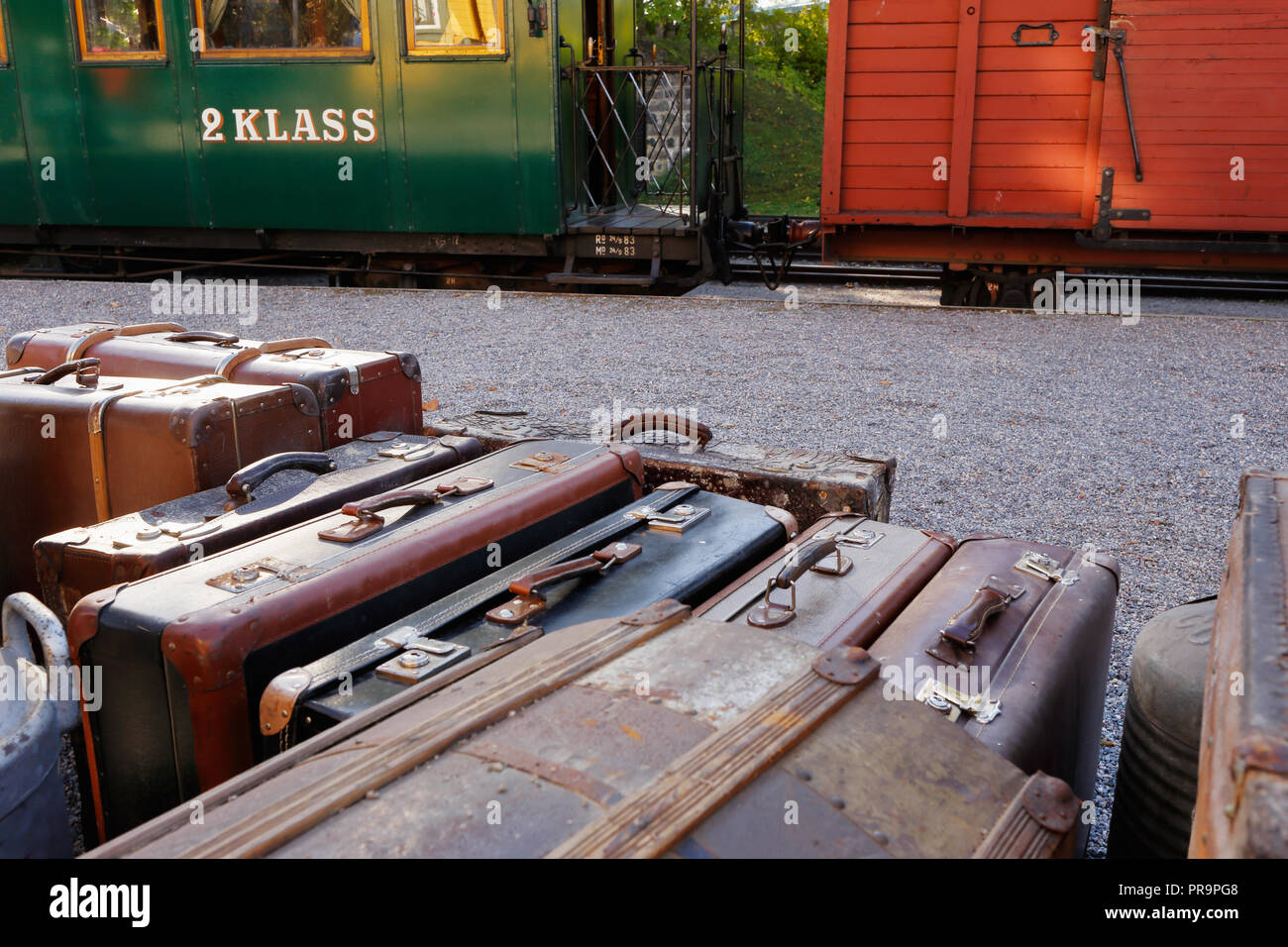 Luggage with suitcases in front of an old train with a wagon and a green second-class passanger wagon. Stock Photo