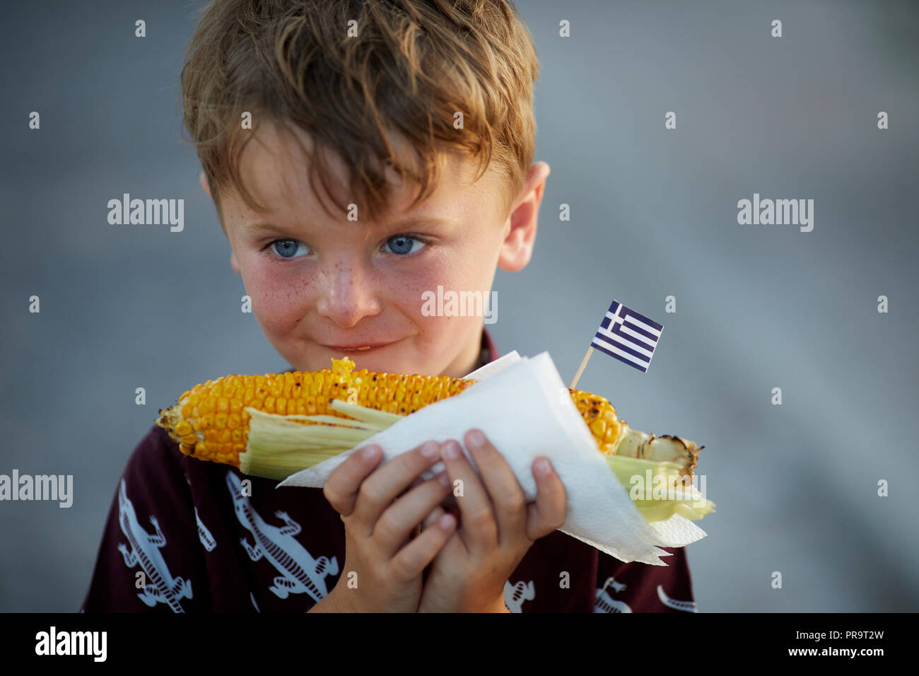 A boy eating Greek street food  corn on the cob in Greece,Santorini, Cyclades group of islands Stock Photo