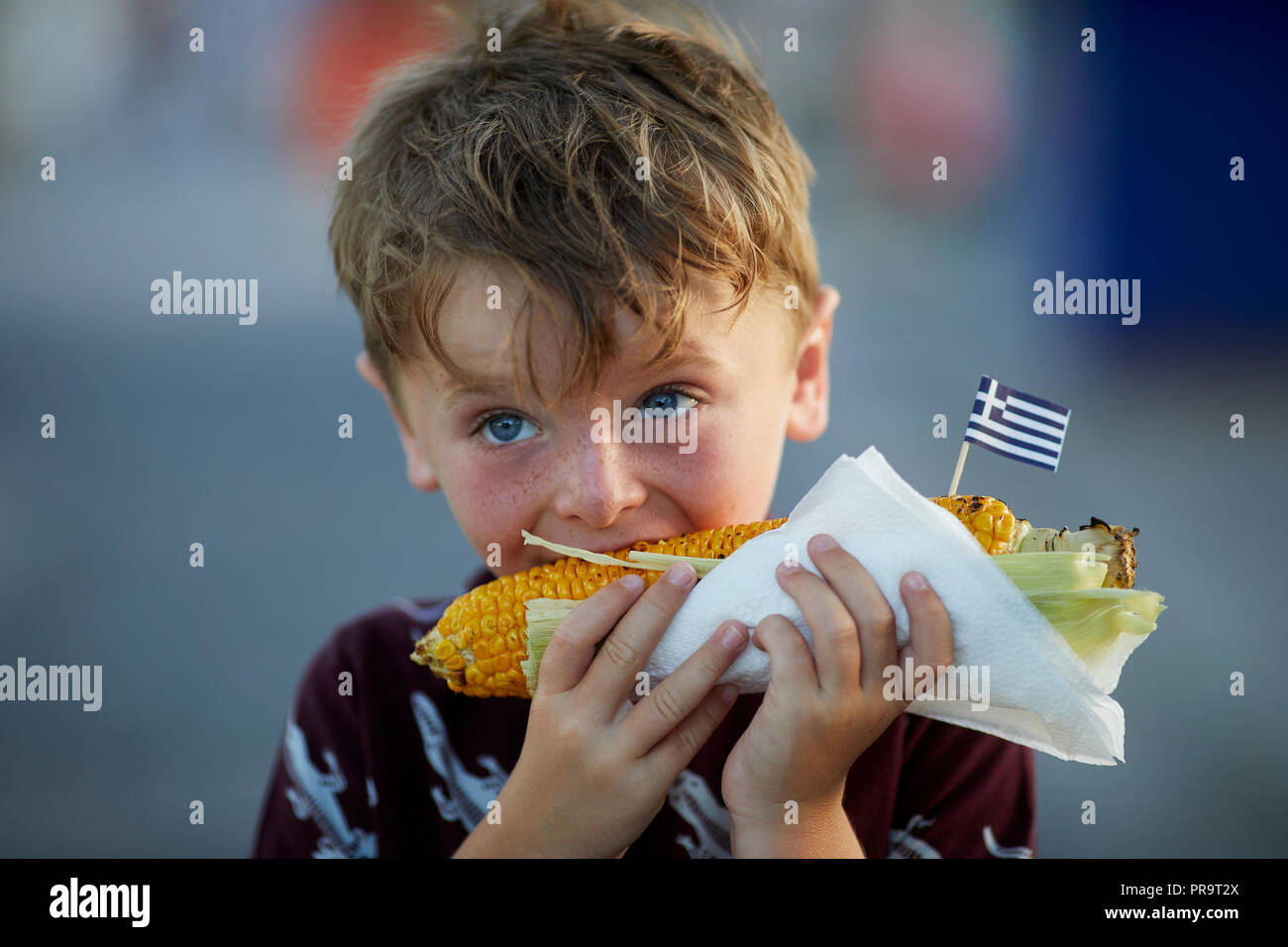 A boy eating Greek street food  corn on the cob in Greece,Santorini, Cyclades group of islands Stock Photo