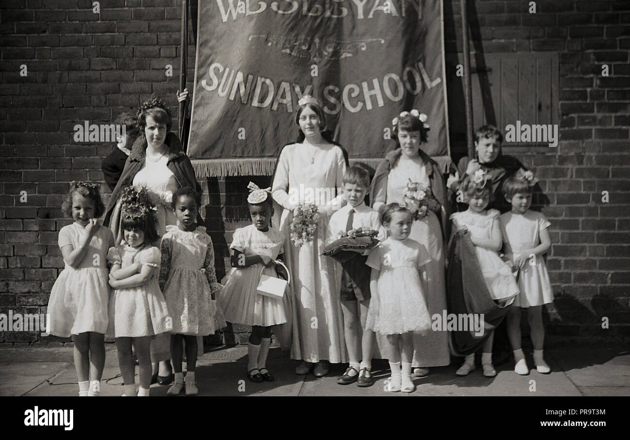 1950s, historical, Sheffield, young children and mothers standing outside in a street under a banner for The Wesleyan Methodist Church Sunday school, before taking part in a parade. Christian in character, a Sunday School was an educational institution, first established in the 1780s in England, to provide an education to working class children and were especially popular in northern english towns, like Manchester and Sheffield. The teaching of the Wesleyan church, called for women’s rights and stood up against child labour. Stock Photo