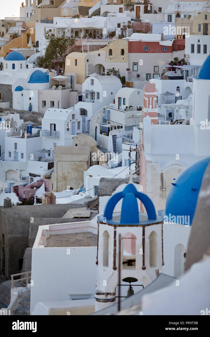 traditional cliff side houses of  Oia landmark blue dome churches Santorini, a Cyclades group of islands in Greece, tourists walking up the steep hill Stock Photo