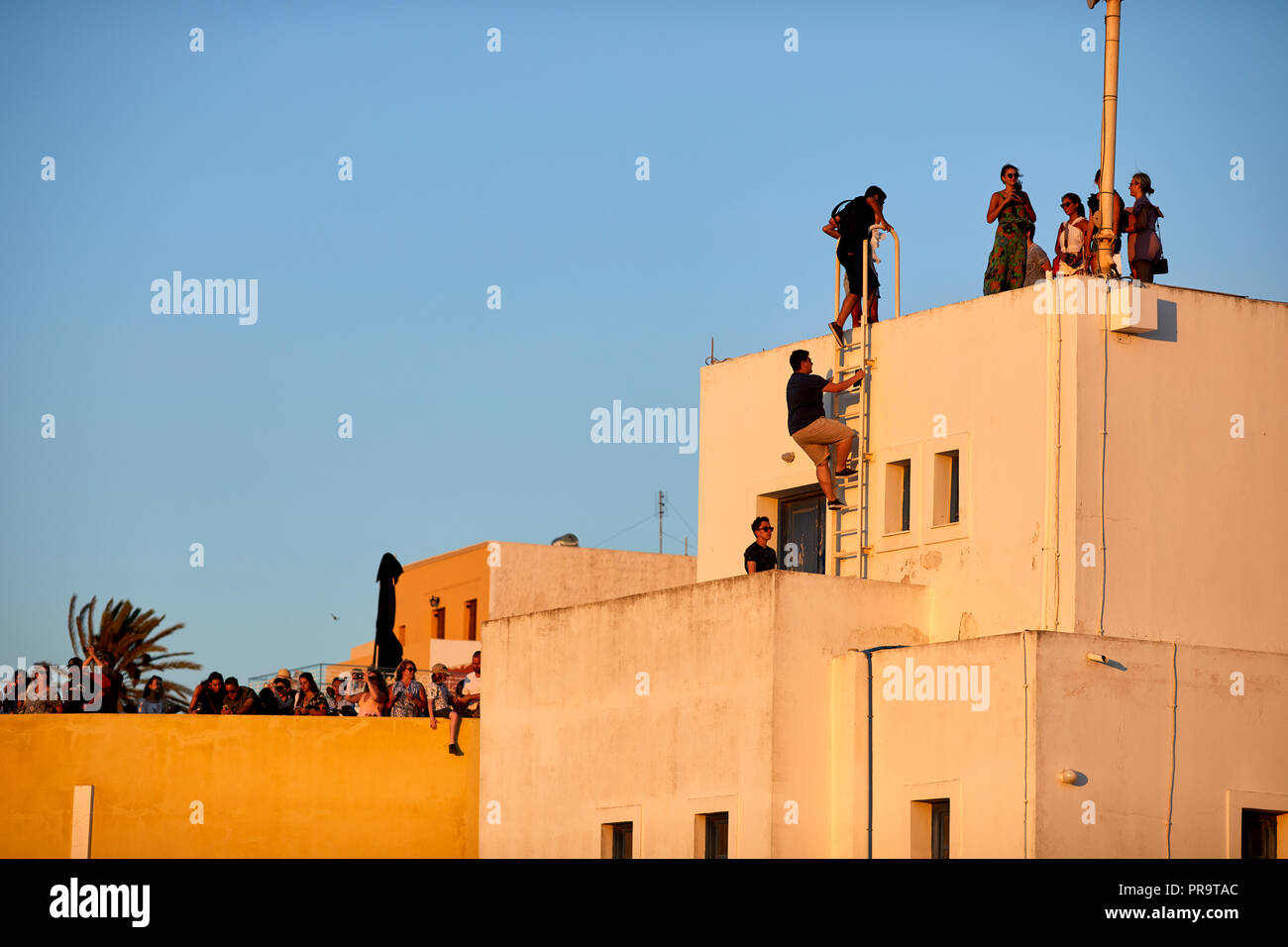 climbing on roof tops getting the best view of the sunset at  Oia landmark windmills Santorini, a Cyclades group of islands in Greece, tourists walkin Stock Photo