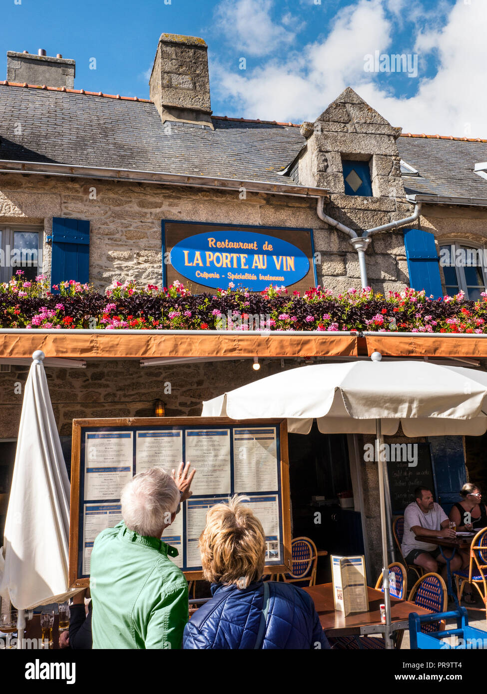 Brittany French alfresco restaurant ‘La Port Au Vin’ with floral display and couple browsing menus Ville Close de Concarneau Bretagne Finistere France Stock Photo