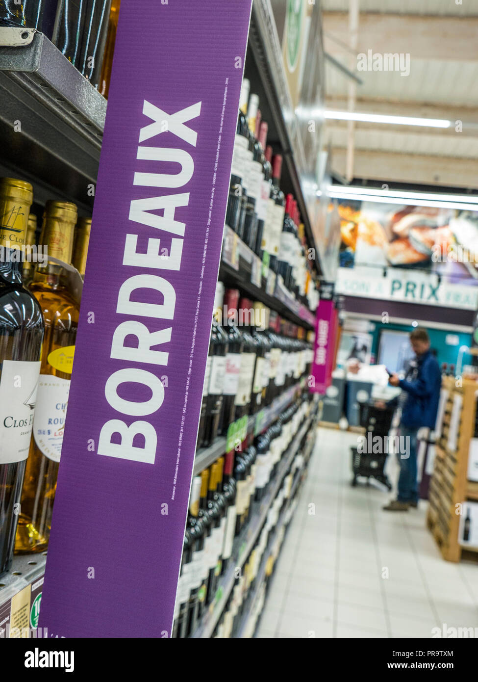 BORDEAUX French wine bottles supermarket aisle with promotional banner in French supermarché, with male shopper browsing the wine varieties France Stock Photo