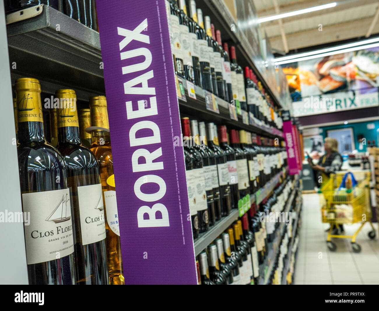 French wine Bordeaux sign bottles supermarket aisle, promotional banner in French supermarket, woman shopper & trolley browsing wine varieties France Stock Photo