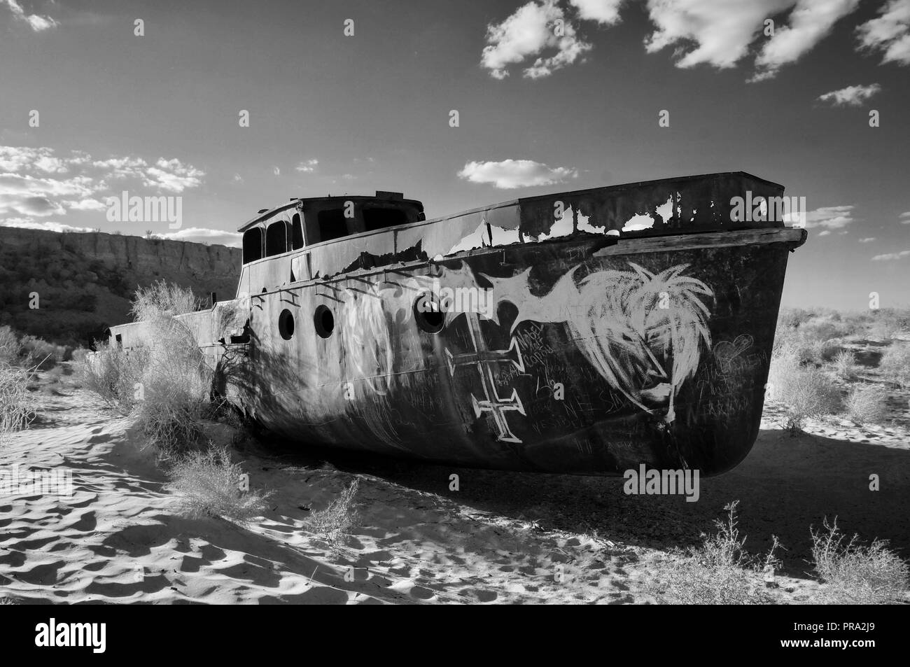 Abandoned solitary ship sits in the desert of what was once the Aral Sea in Uzbekistan. Black and white Stock Photo