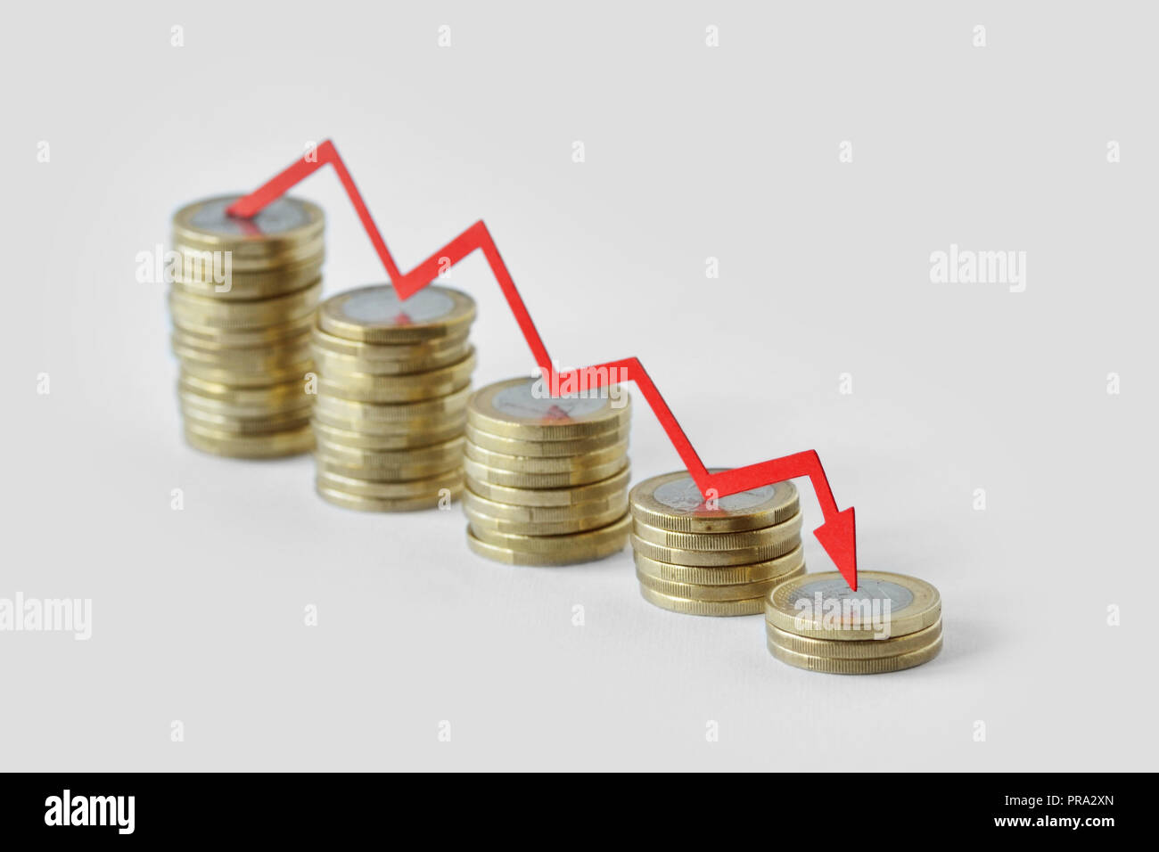 Piles of coins with red decreasing arrow - Loss of money concept Stock Photo