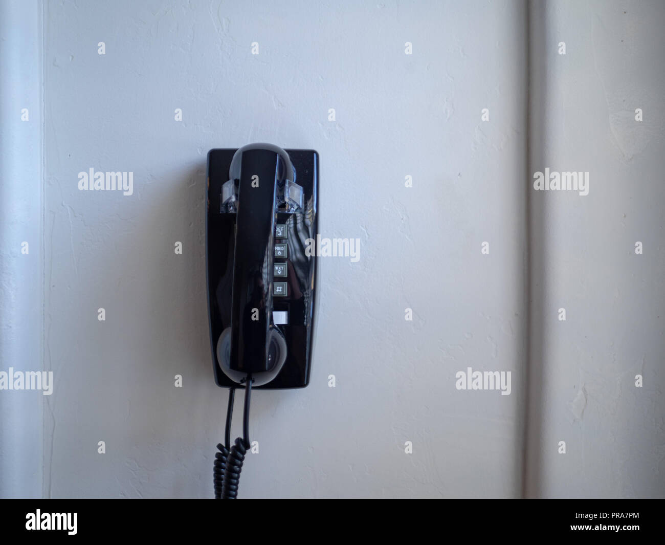 Black landline phone and receiver hanging on white wall Stock Photo Alamy