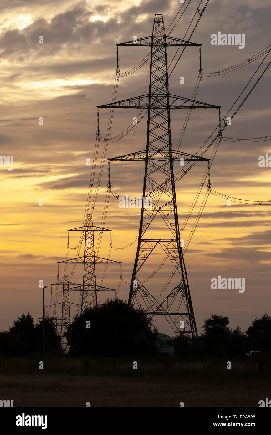 Electricity pylons or transmission towers carrying high voltage power lines and overhead cables above land as part of the national grid network supply Stock Photo