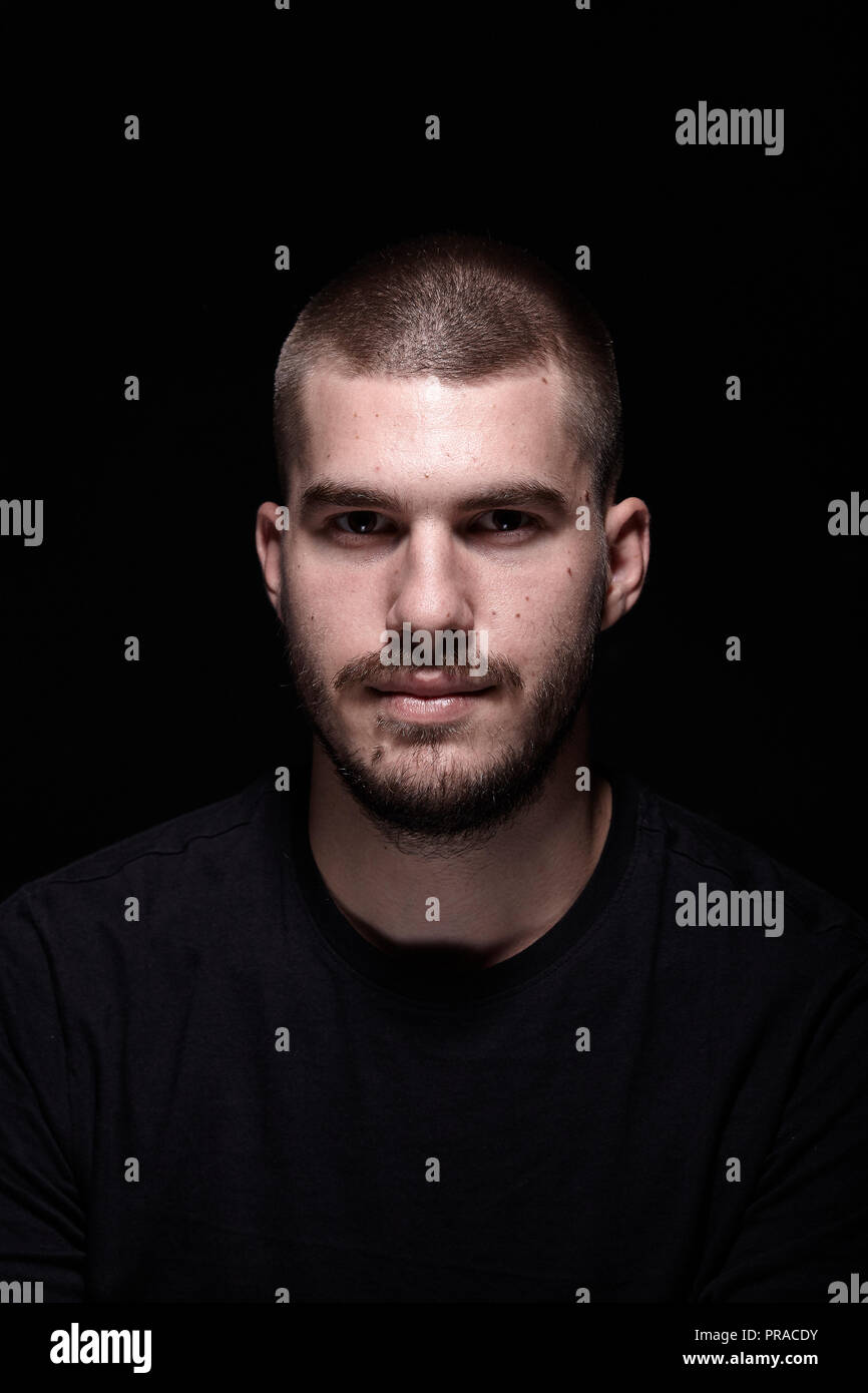 one young man, dramatic portrait. black background. head and shoulders shot. looking at camera