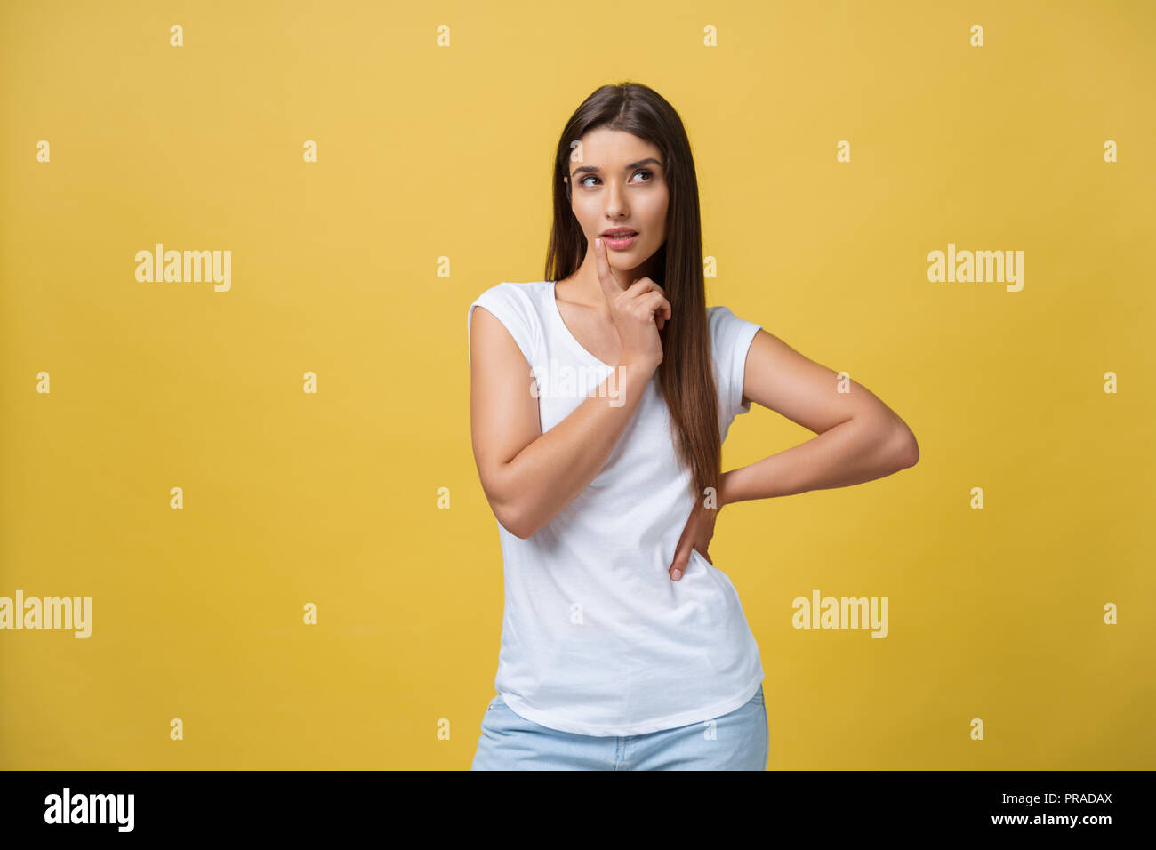 portrait of the beautiful young woman thinking on the yellow background ...