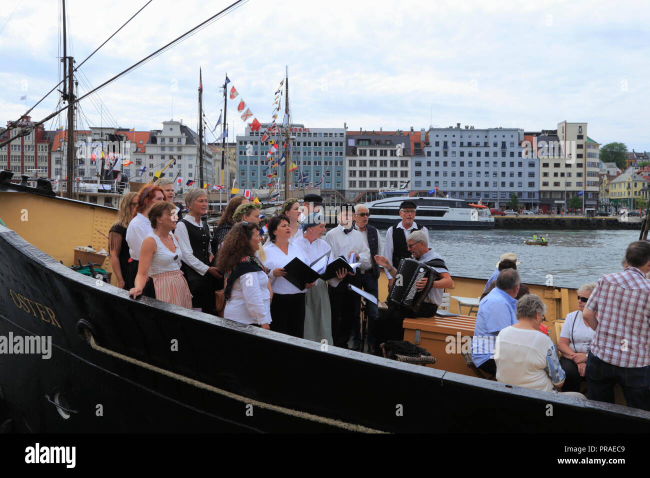 A choir performs traditional Norwegian songs and folk music on the deck of a boat in Bergen harbour, Norway, during Market Day (Torgdagen). Stock Photo