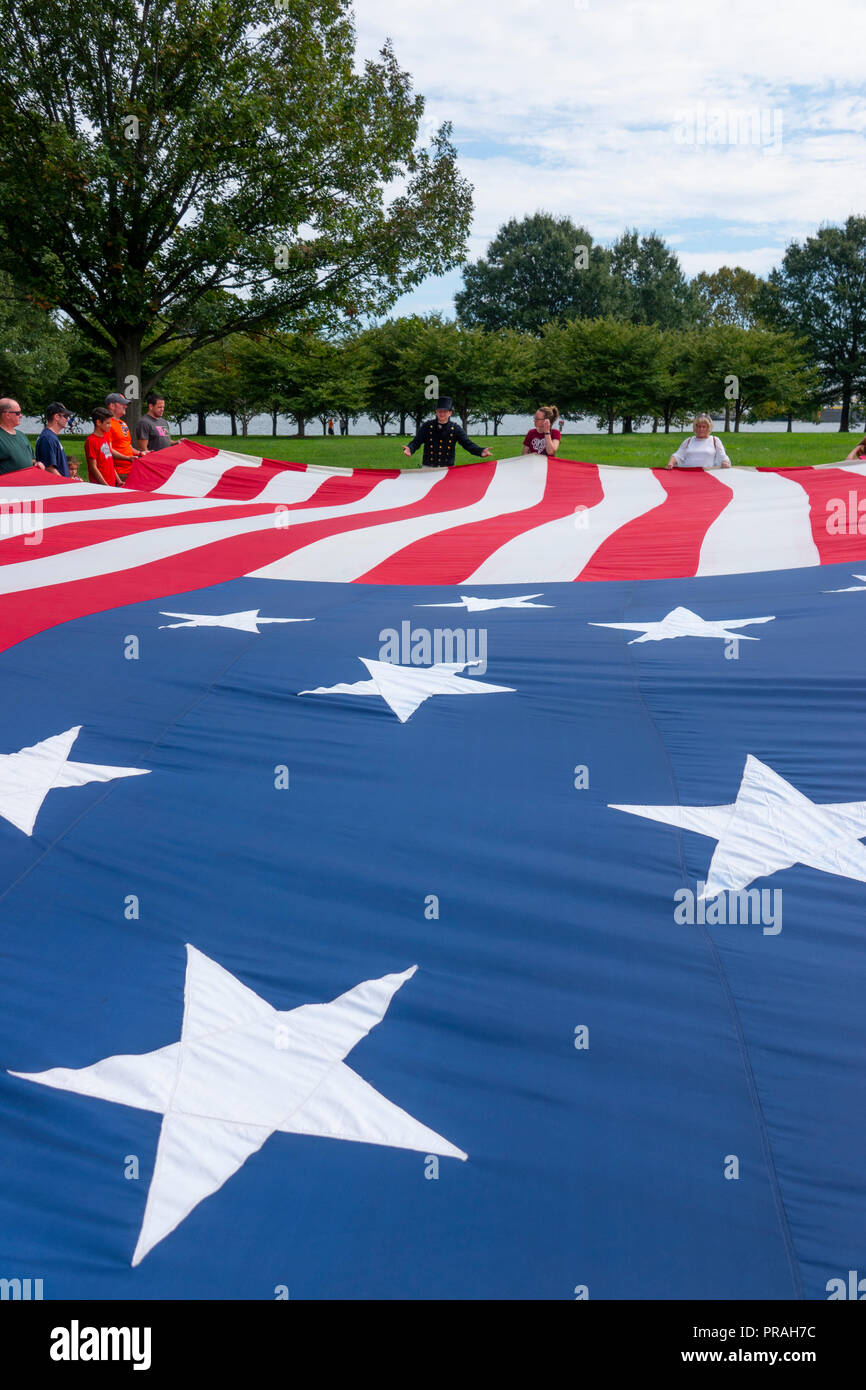USA Maryland MD Baltimore Fort McHenry visitors hold up a large replica of the flag that was flying when Francis Scott Key wrote the Anthem poem Stock Photo