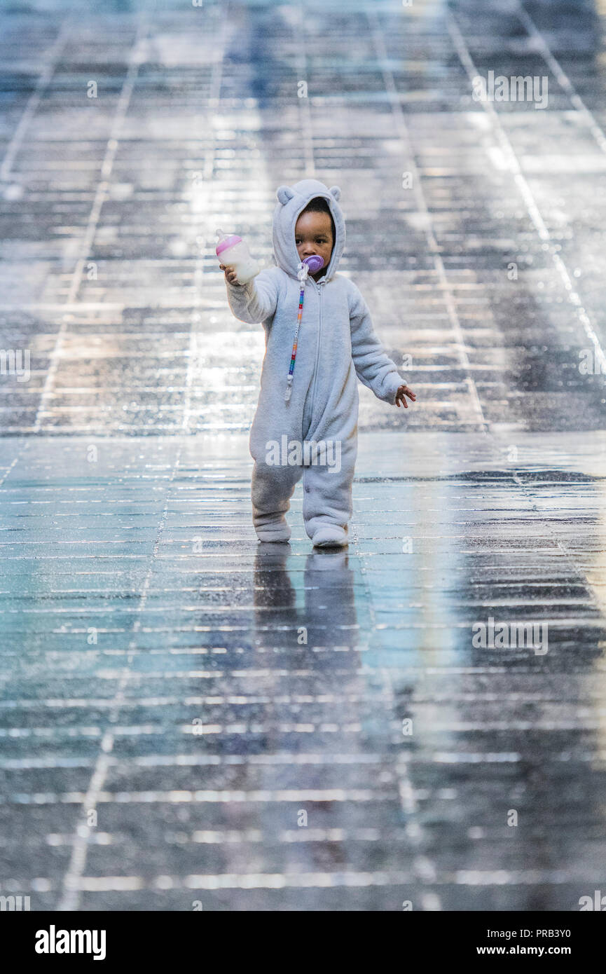 London, UK. 1st Oct 2018. Natalie Bell's granddaugter enjoys the reflective flooring in the entrance - Hyundai Commission: Tania Bruguera is at Tate Modern - a work built around migration using a heat sensitive floor.  As part of the overall installation she collaborated with 21 local people including Natalie Bell, a local activist honoured for her work in the community by having the Boiler House renamed after her.  A large-scale, interactive and multi-faceted commission within Turbine Hall from 2 October 2018 to 24 February 2019. Credit: Guy Bell/Alamy Live News Stock Photo
