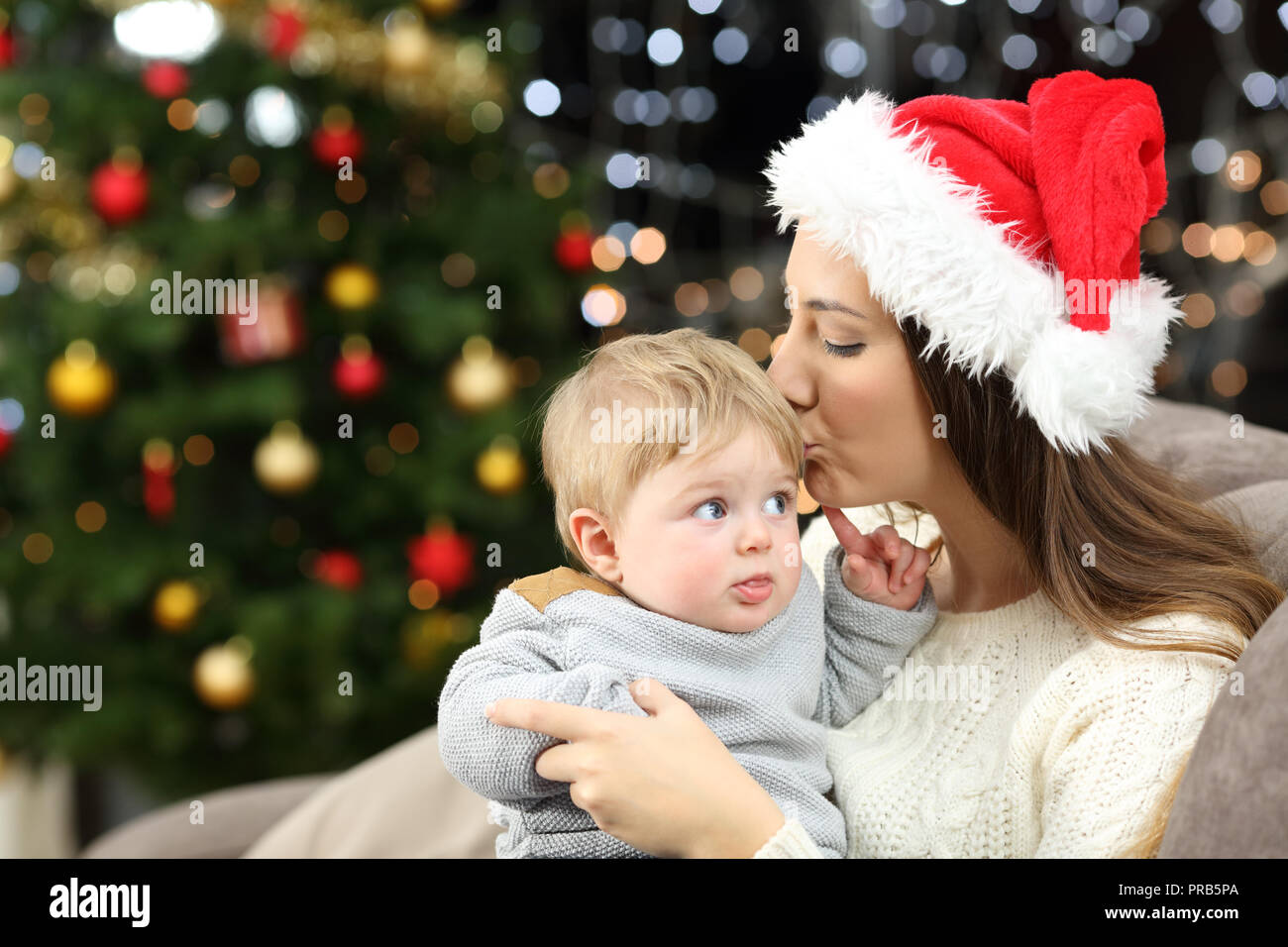 Affectionate mother kissing her baby son in christmas sitting on a couch in the living room at home Stock Photo