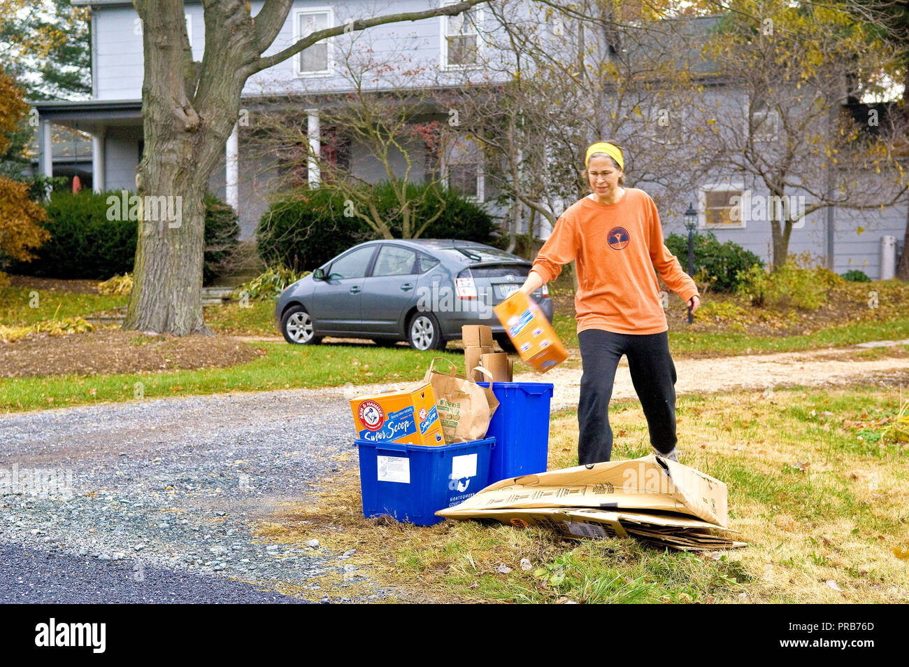 2007 - Woman taking trash out to a recycle bin along the street in front of her home. Stock Photo