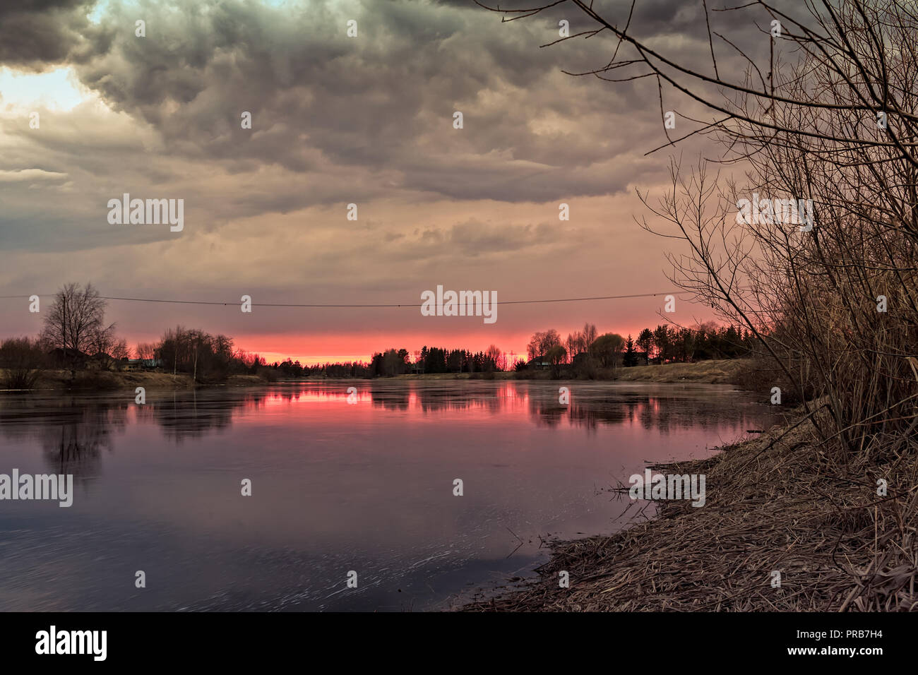 The sun sets behind the river bend and colors the dramatic clouds of