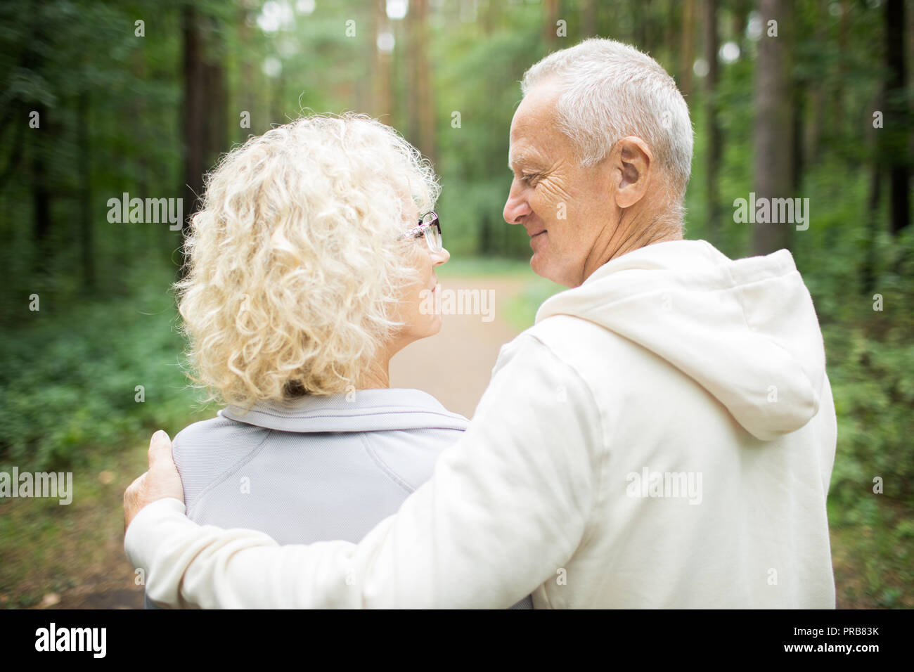 Back view of senior couple walking down in embrace in the forest on summer day Stock Photo