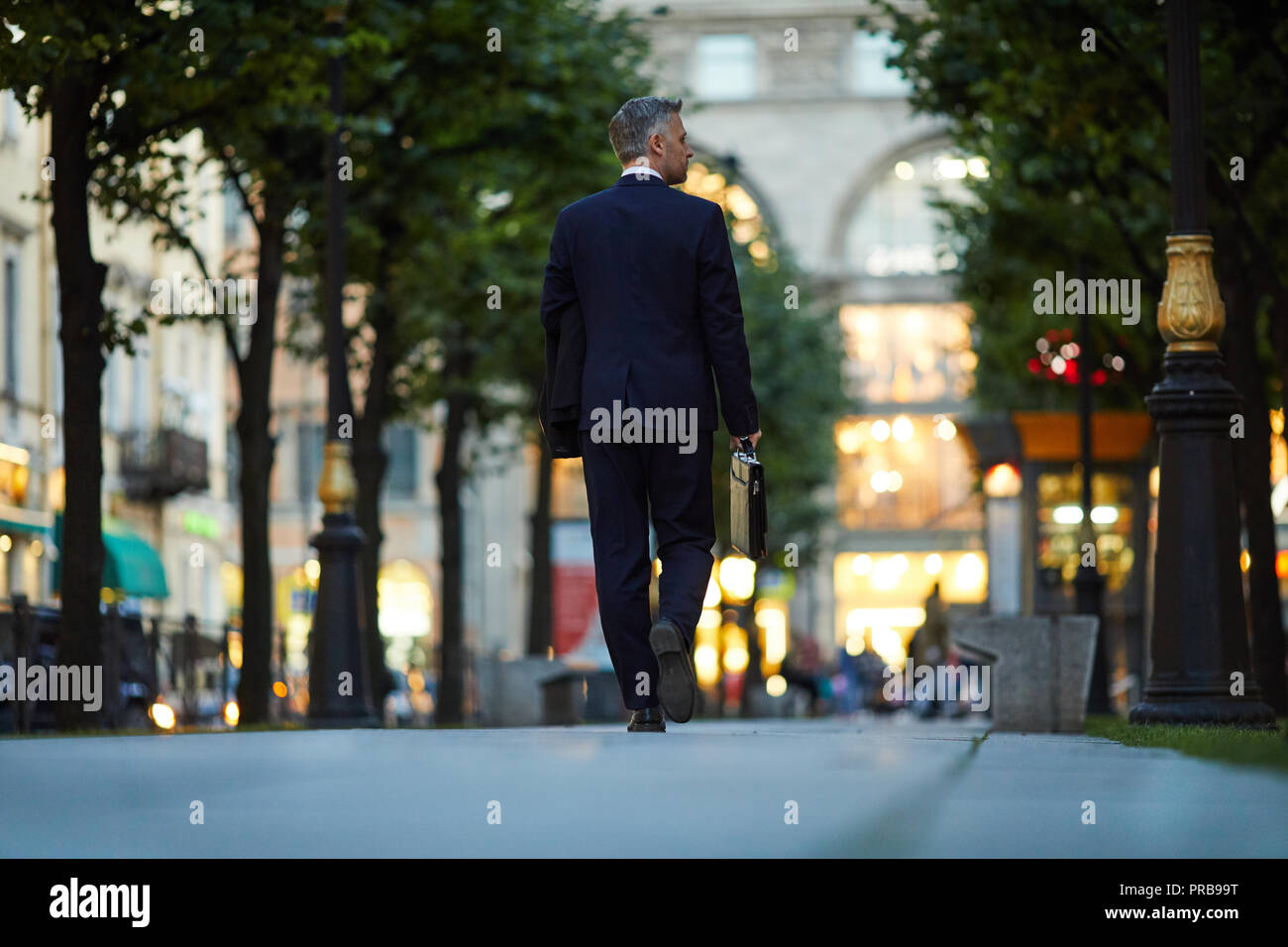 Back view of elegant man in suit with briefcase and coat walking down