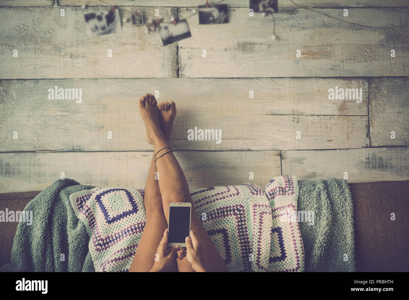 Woman lying on the couch with legs resting on the wall relaxes looking at the phone Stock Photo