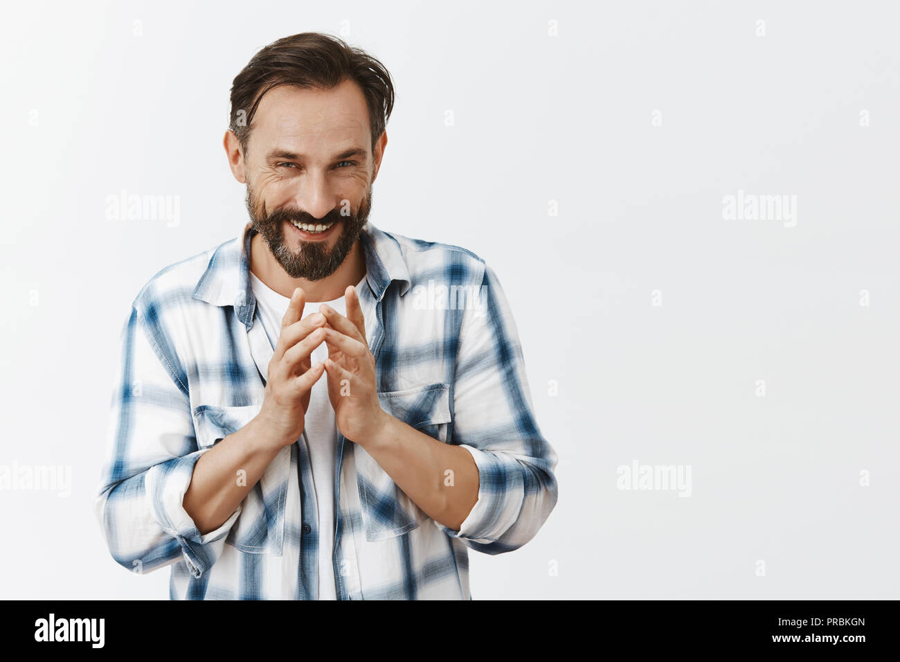Adult evil genius making mysterious plan, steepled fingers in front of chest and smiling with scorn and arrogant expression, being self-assured in plan, standing over gray background Stock Photo