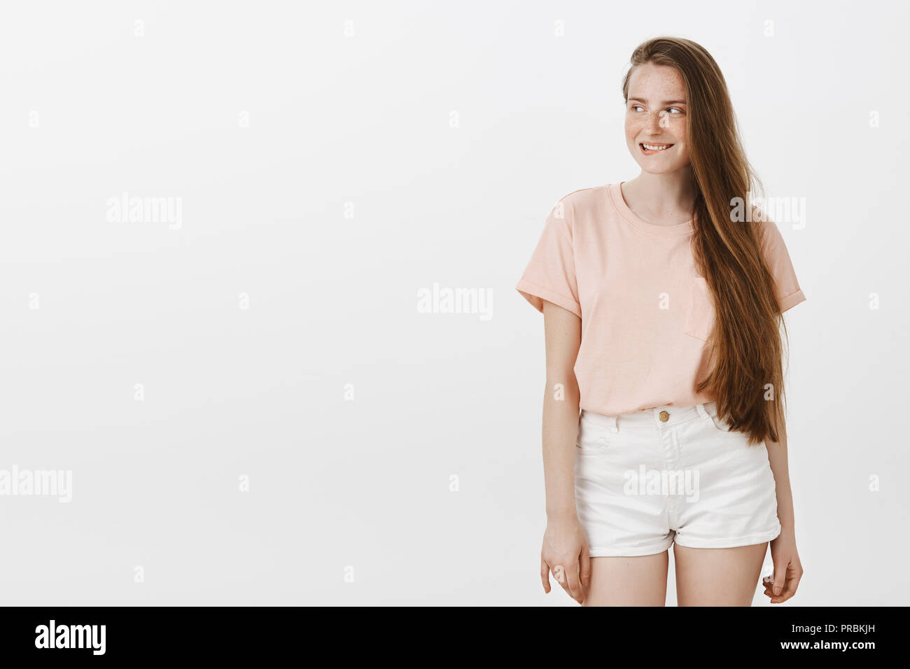 Indoor shot of amused attractive female feeling intrigued, having some interesting intention in mind, smirking while gazing left with curiosity, standing over gray background in stylish clothes Stock Photo