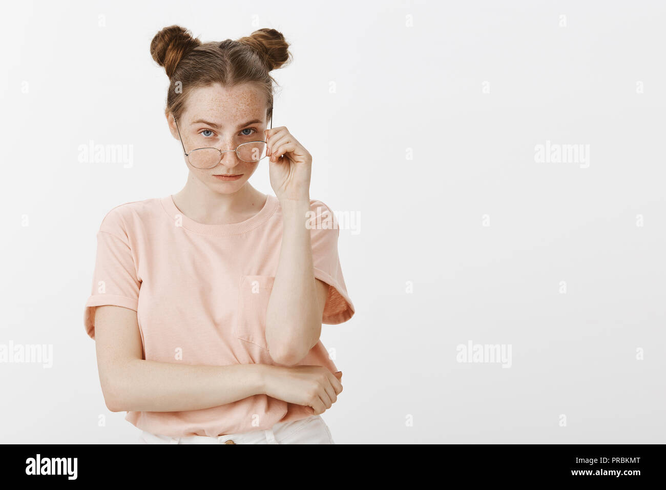 Are you sure about it. Portrait of uncertain beautiful female with buns hairstyle and freckles, taking off glasses and staring doubtfully at camera, being unsure, expressing hesitation and interest Stock Photo