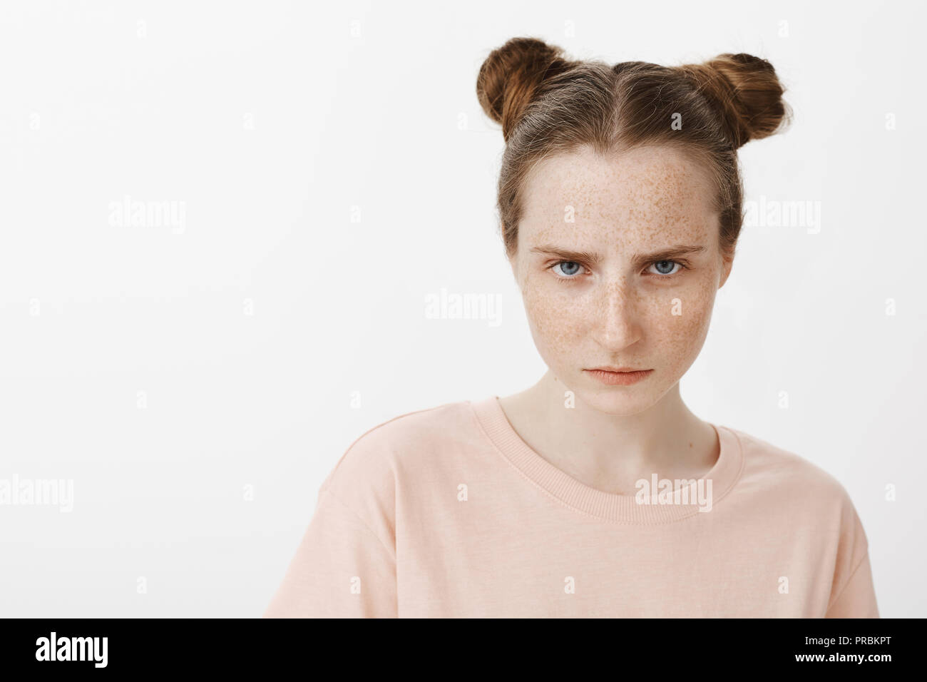 Girl looking at enemy, feeling scorn and anger, looking from under forehead at camera and frowning, standing serious and outraged over gray background, having bad day in school Stock Photo