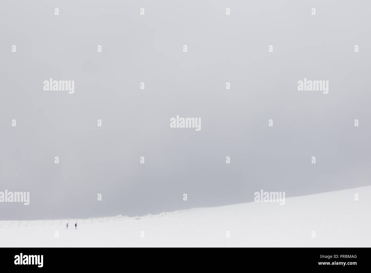 A very minimalistic view of two distant people over a mountain covered by snow, near a fence Stock Photo