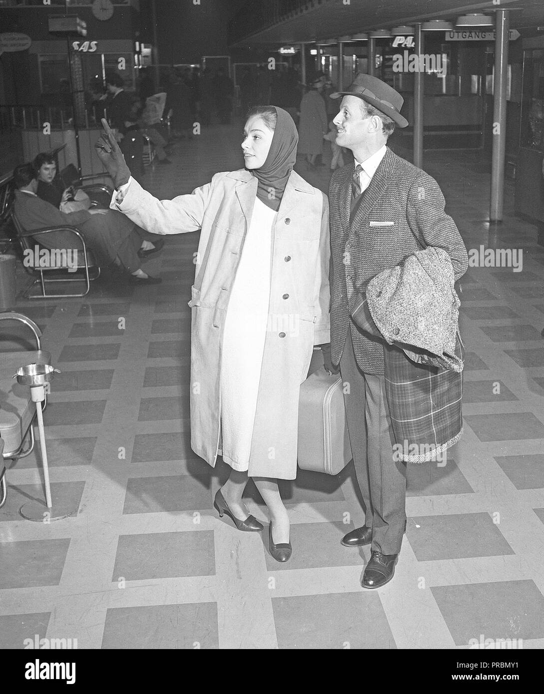 Couple in the 1950s. A young couple in an airport, ready for their holiday trip, carrying their luggage in the departure terminal. She is pointing at something in the terminal, perhaps she has found the boarding gate or the departure time on a sign.  Sweden 1956. Photo Kristoffersson Ref CB15-9 Stock Photo