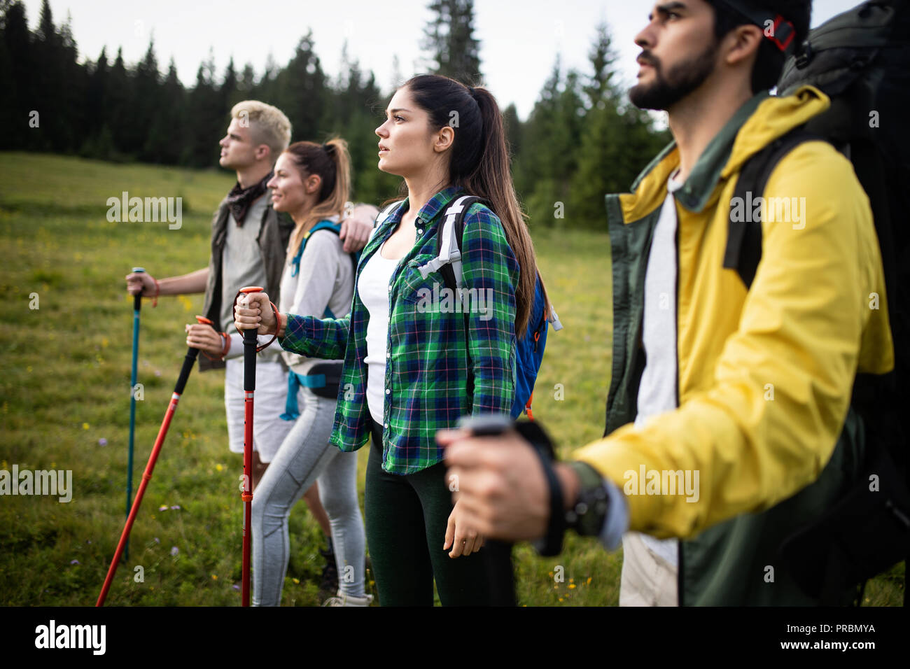 Group of hikers with backpacks and sticks walking on mountain. Friends making an excursion Stock Photo