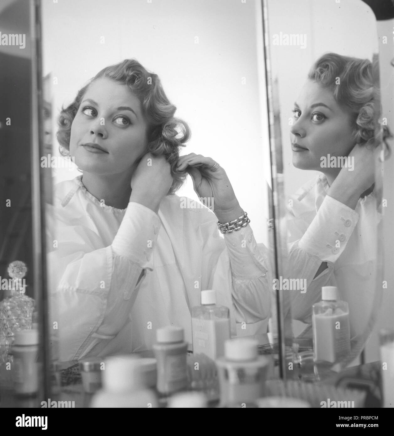 Makeup in the 1950s. A young blonde girl is fixing her hair in front of the mirror. Sweden April 1954 Stock Photo