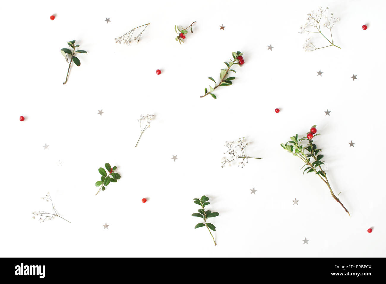 Christmas floral pattern. Winter composition of red cranberry branches, baby's breath flowers and silver confetti stars on white table. Festive background. Flat lay, top view. Stock Photo