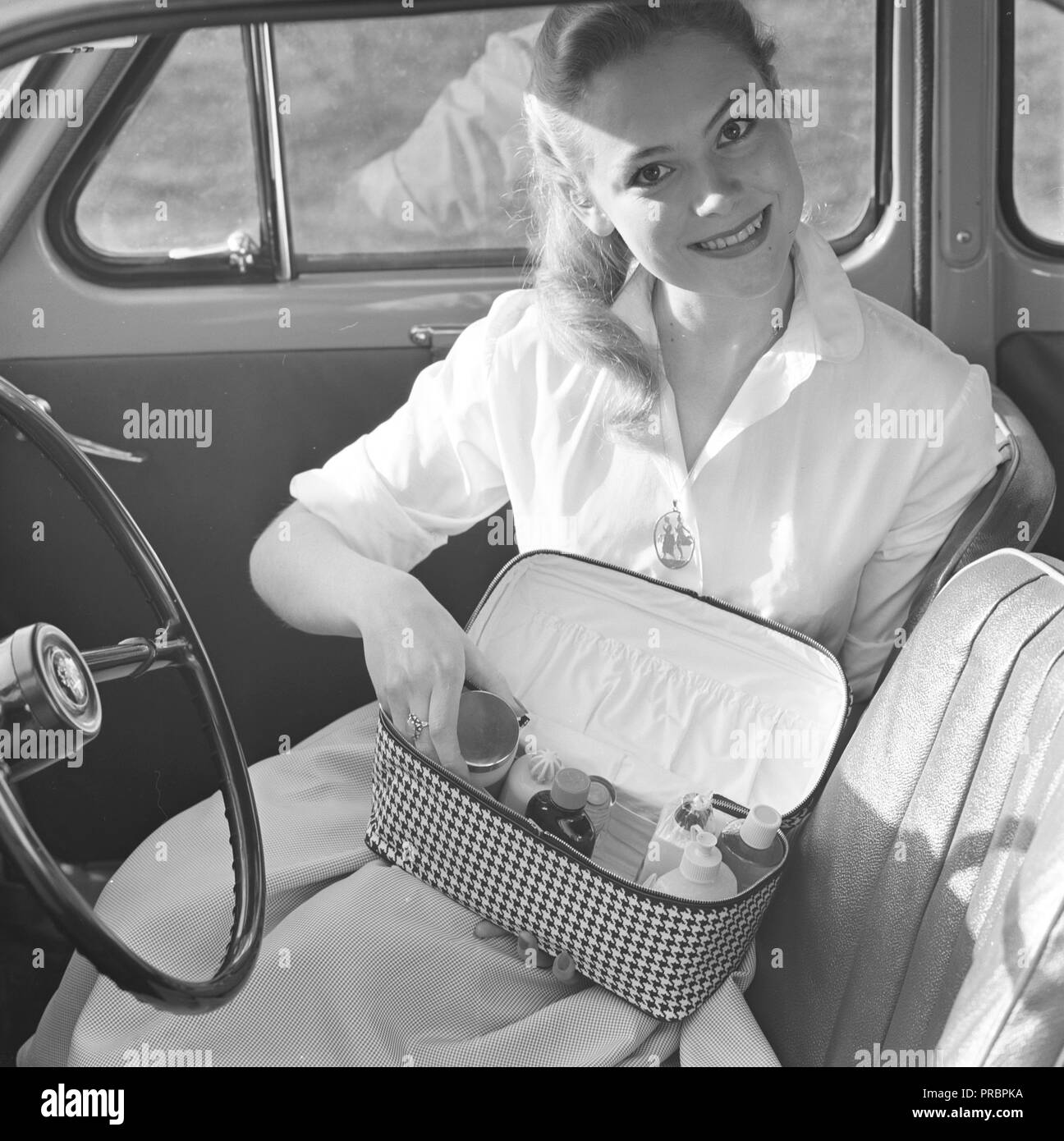Makeup in the 1950s. A young blonde woman in a car is showing her practical makeup bag that contains perfumes, lotions and cosmetics. Sweden 1957 Stock Photo