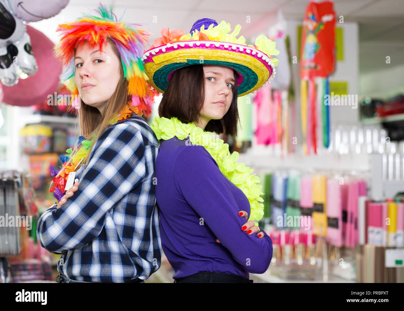 Portrait of comically dressed cheerful girls with crossed hands standing back to back in festive things shop Stock Photo