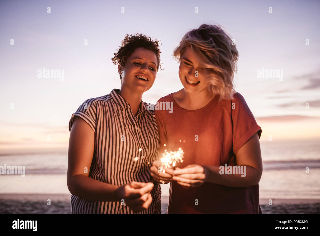 Laughing female friends playing with sparklers during a beach sunset Stock Photo