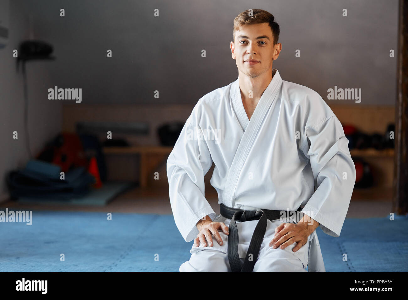 Karate man in kimono sits on knees on floor in martial arts gym Stock