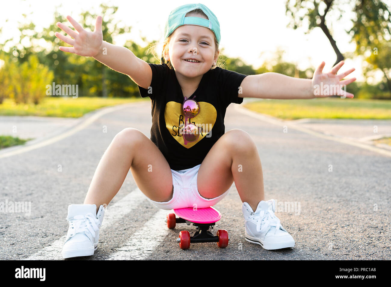 Child riding skateboard in summer park. Little girl learning to ride