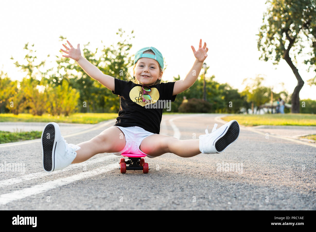 Child riding skateboard in summer park. Little girl learning to ride