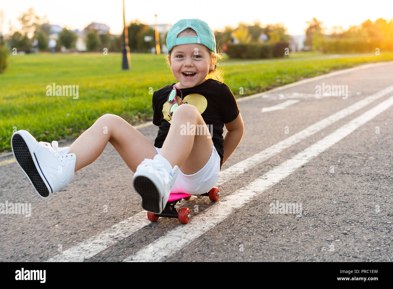 Child riding skateboard in summer park. Little girl learning to ride