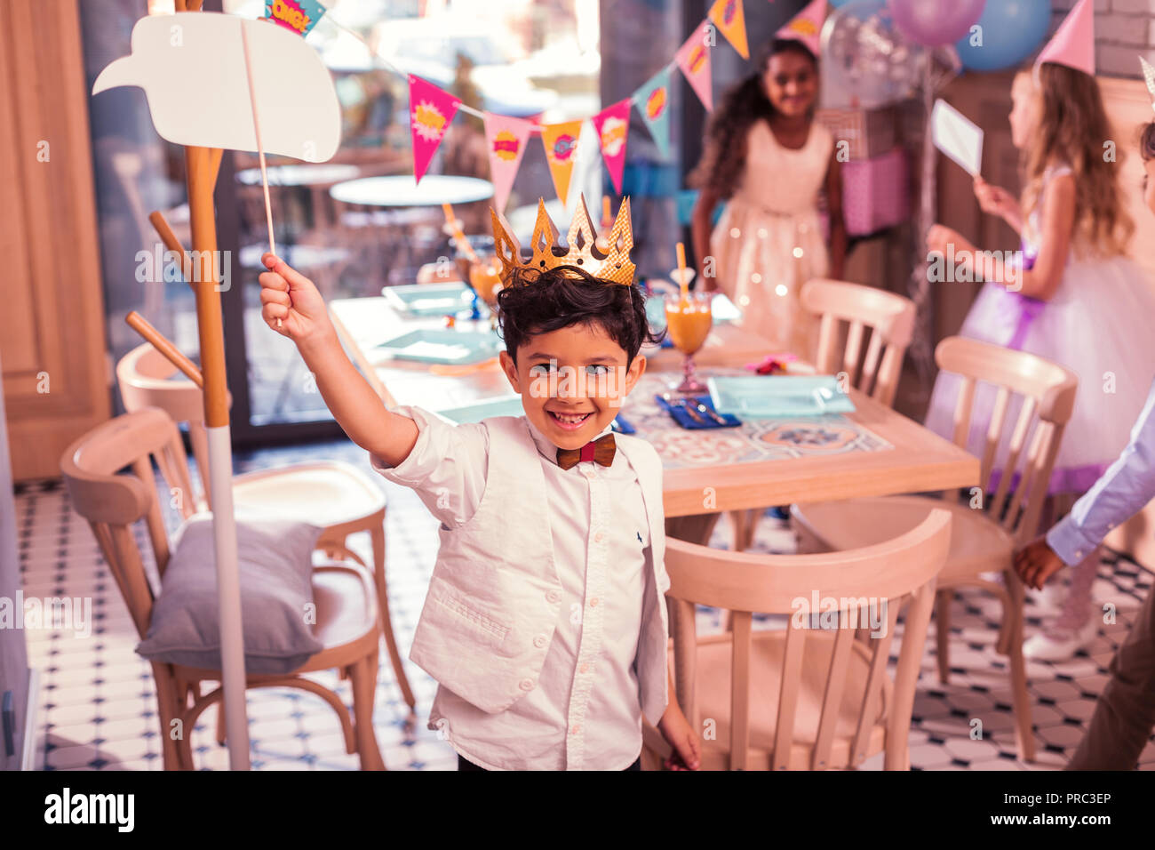 Little boy wearing paper crown and putting hand up at the party Stock Photo