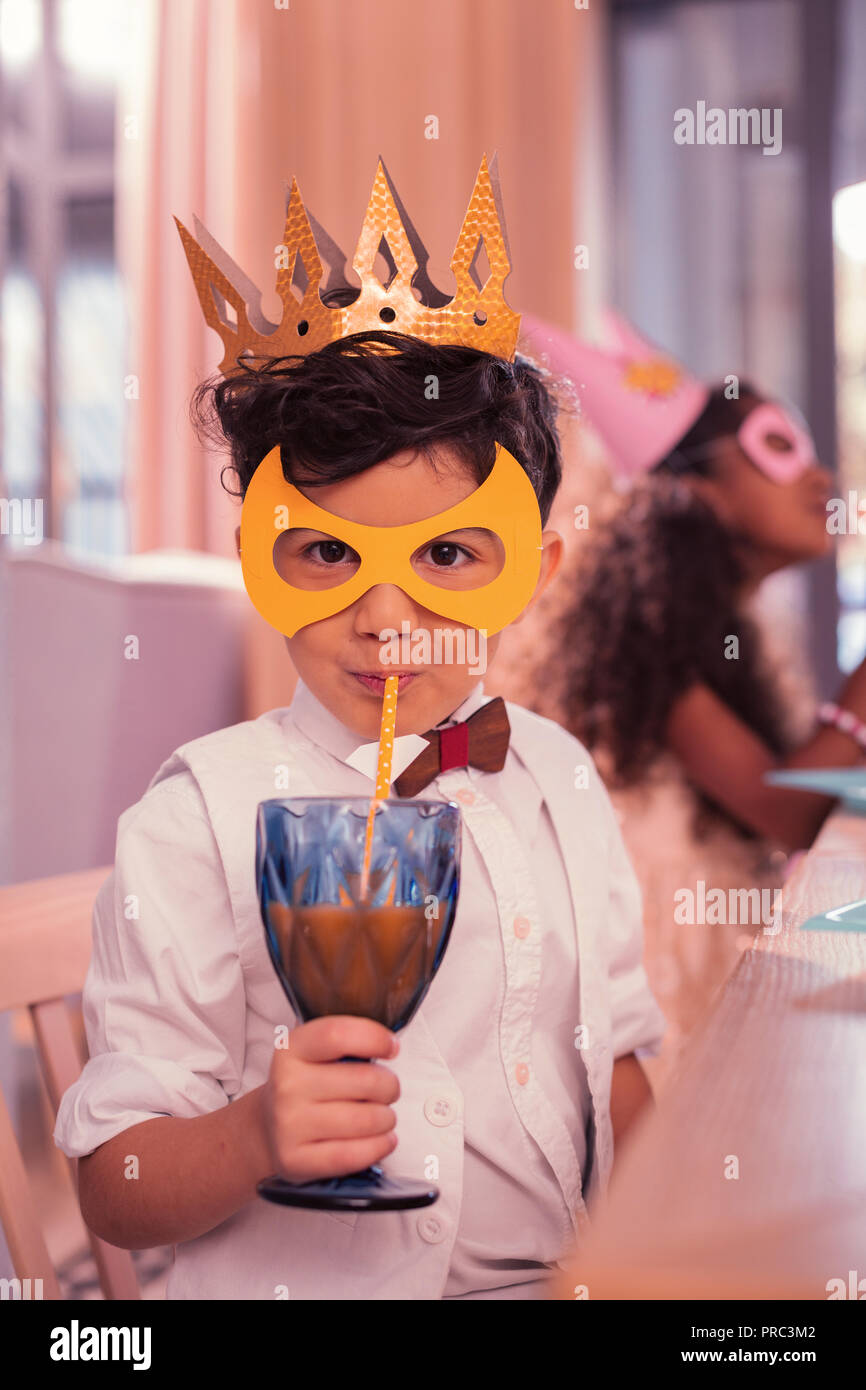 Little boy drinking juice with sipping straw while being at masquerade Stock Photo